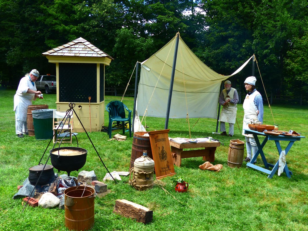 men wearing historical clothing and demonstrating historical process of making beer