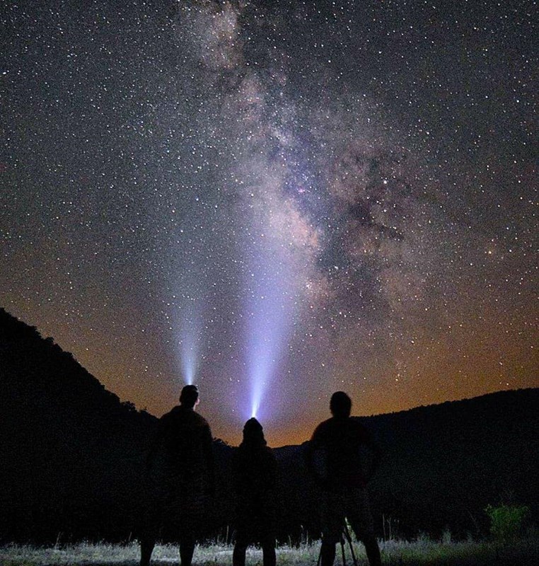 Silhouette of three hikers wearing headlamps gazing up at a starry night sky