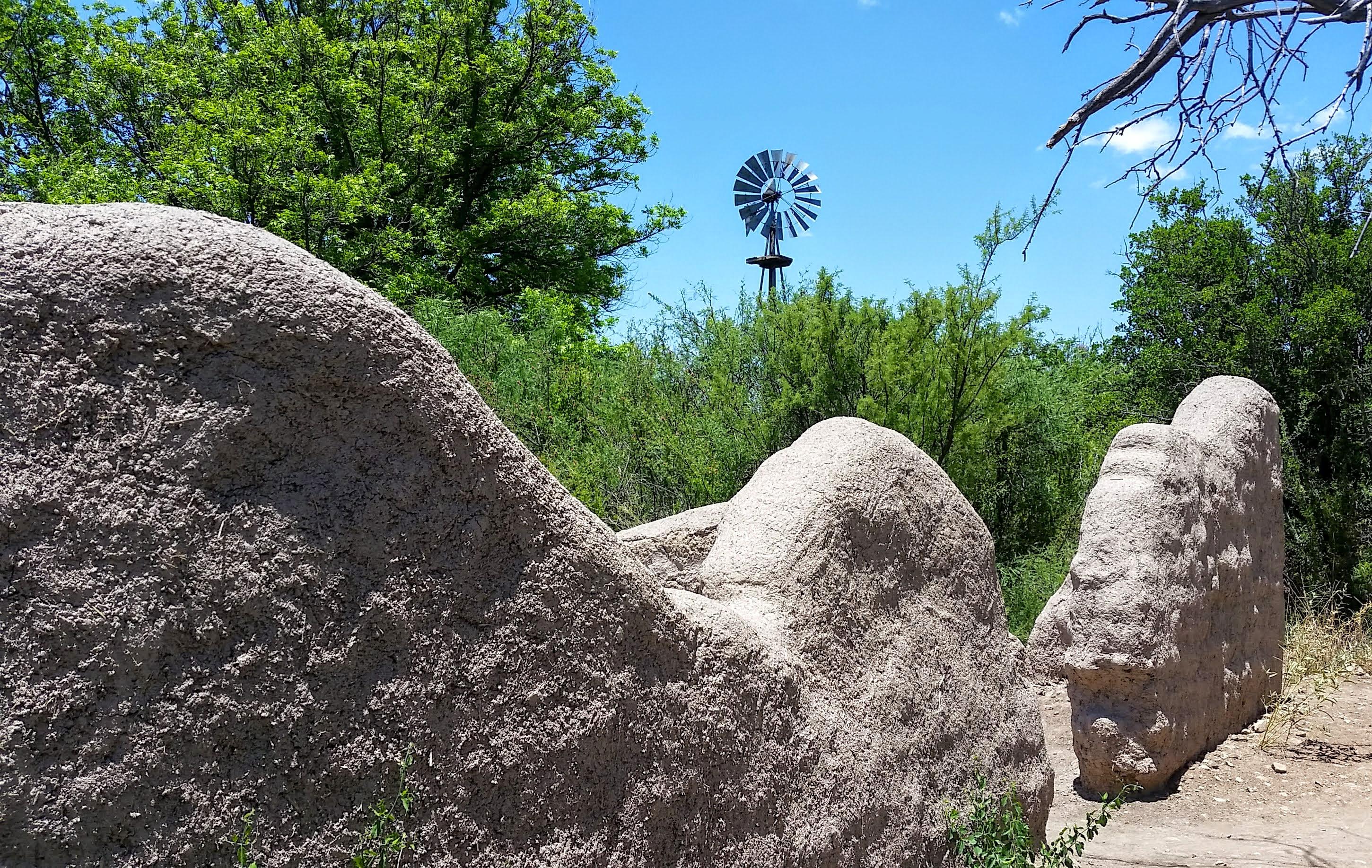A windmill rises above the half-ruined walls of an adobe structure.