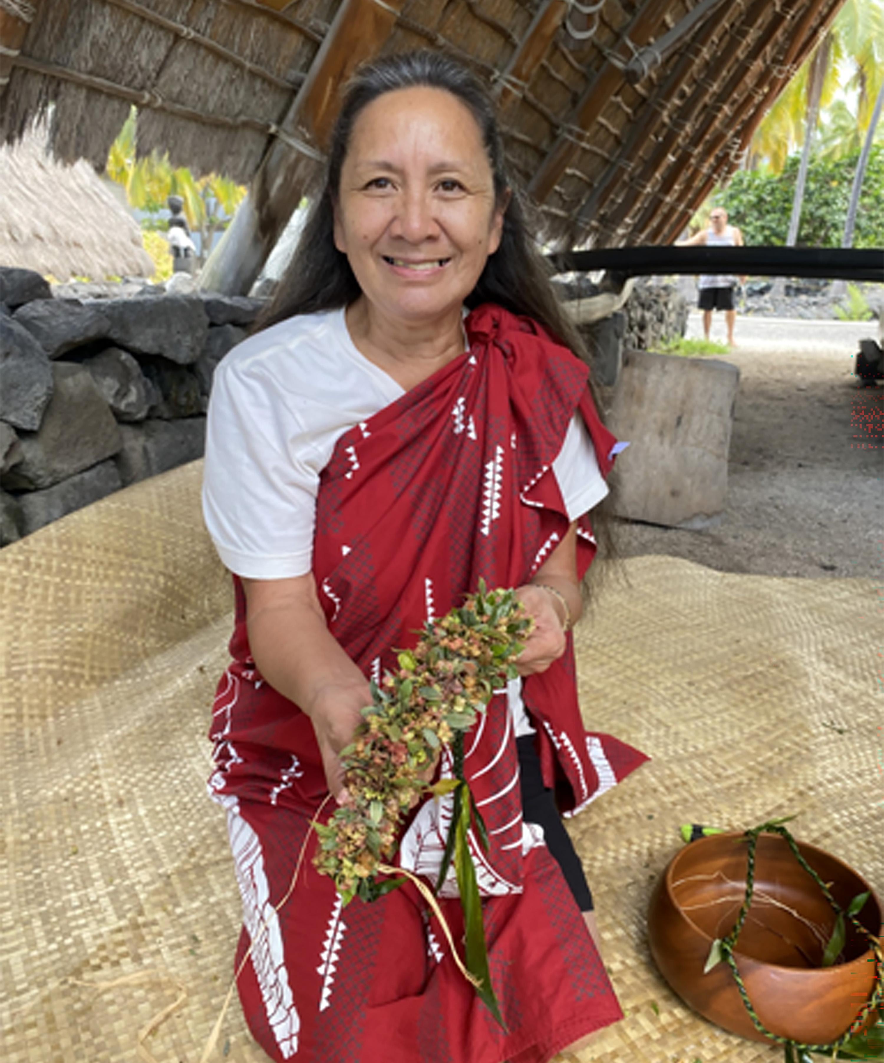 Woman holding hana lei underneath traditional Hawaiian halau