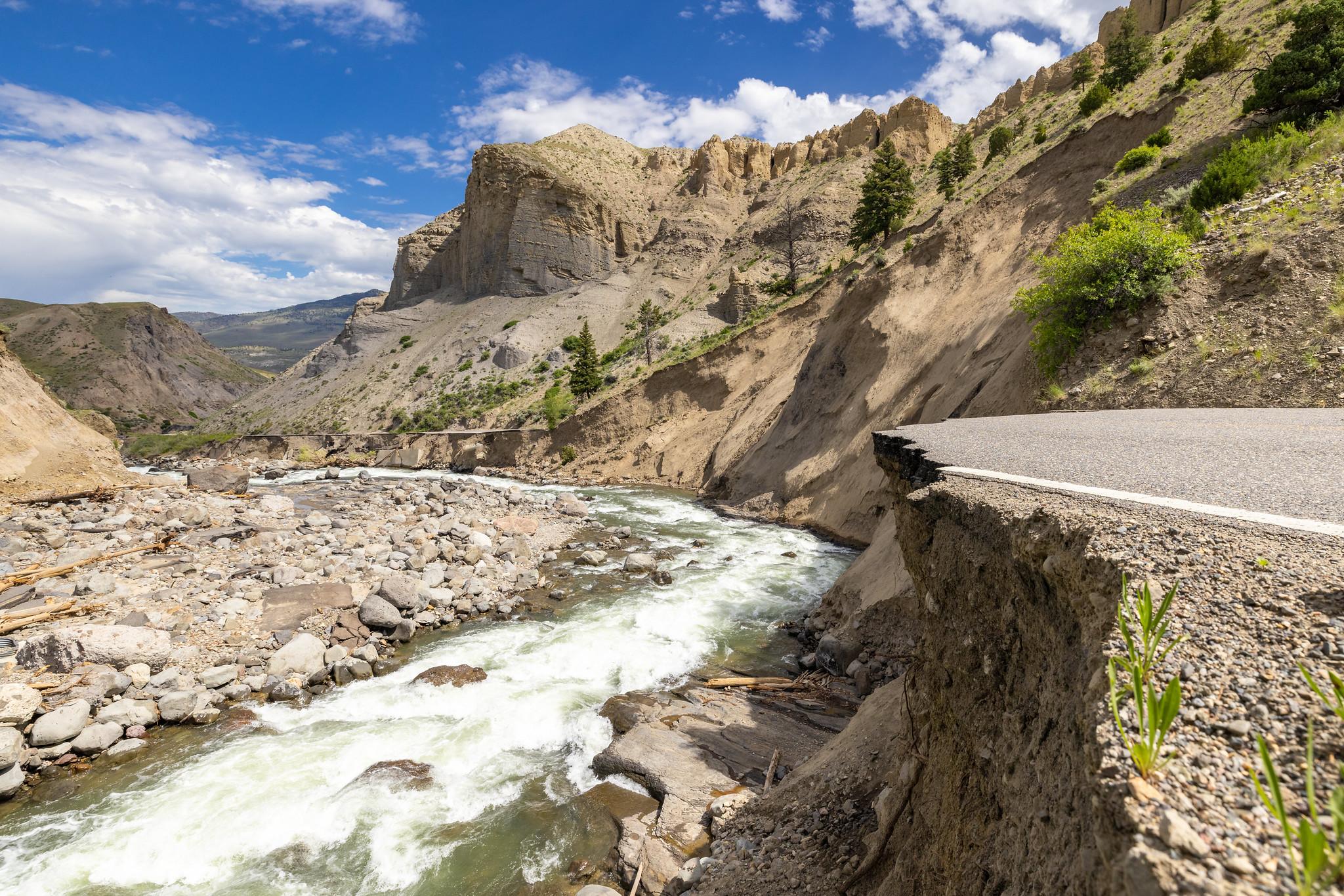 A river meandering through a deep canyon surrounded by cliffs near a damaged roadway