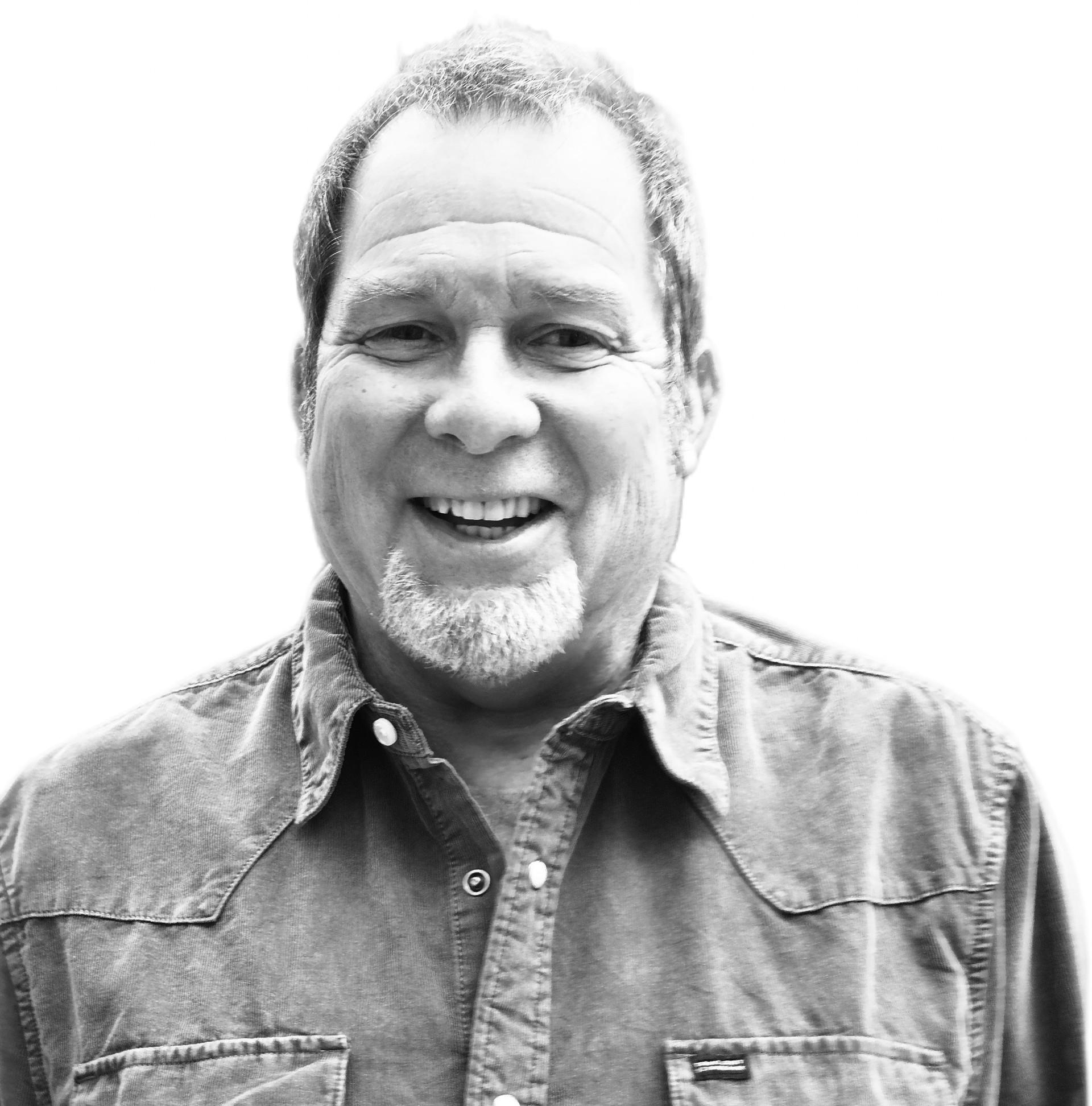 A black and white image of a middle-aged, smiling white man pictured from the chest up.