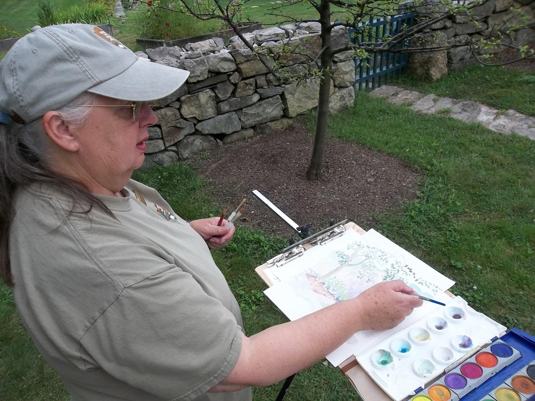 A painter with a hat on paints with watercolors.