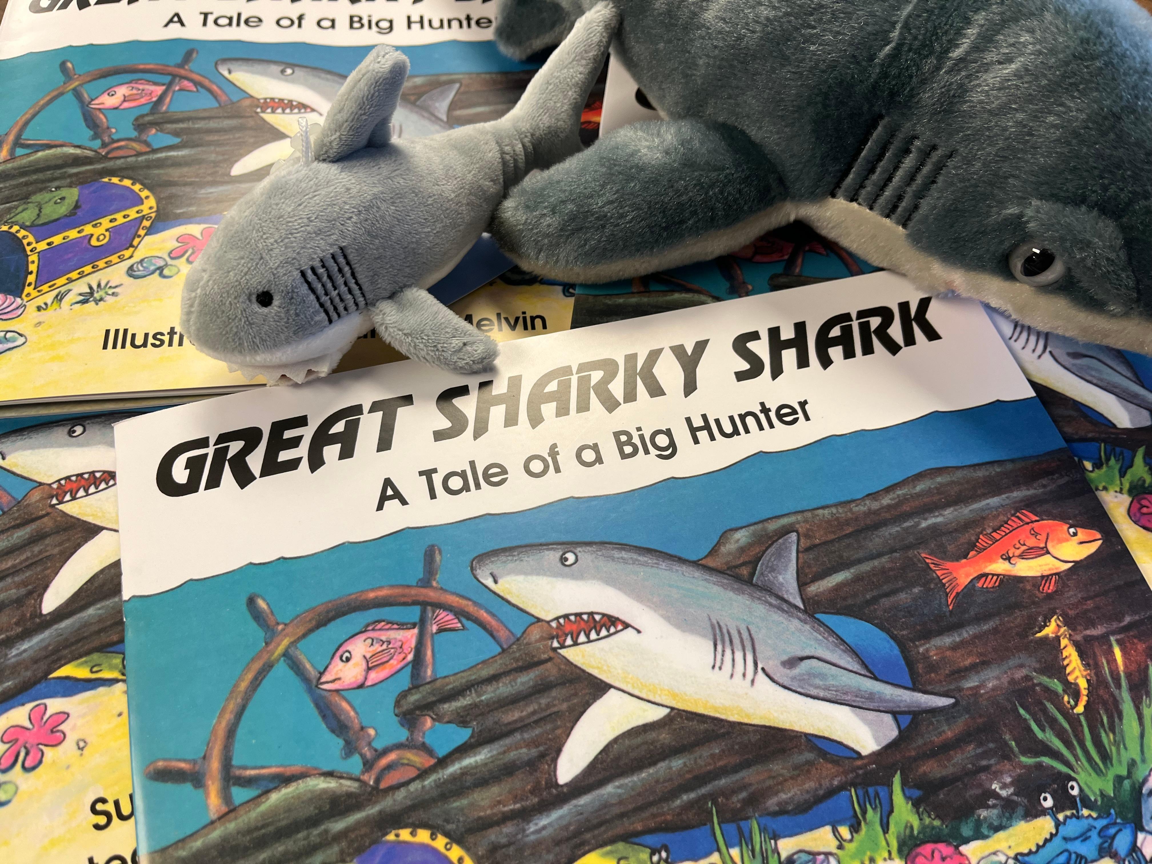 A stuffed animal shark on top of a book about sharks.