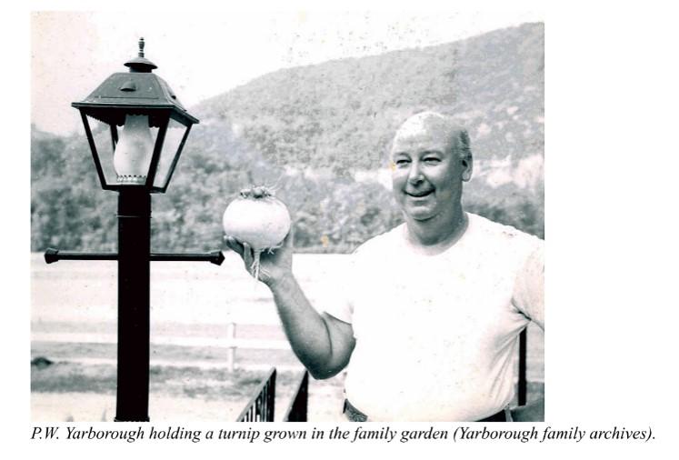 A black and white image of a man holding up a turnip standing next to a lantern post.