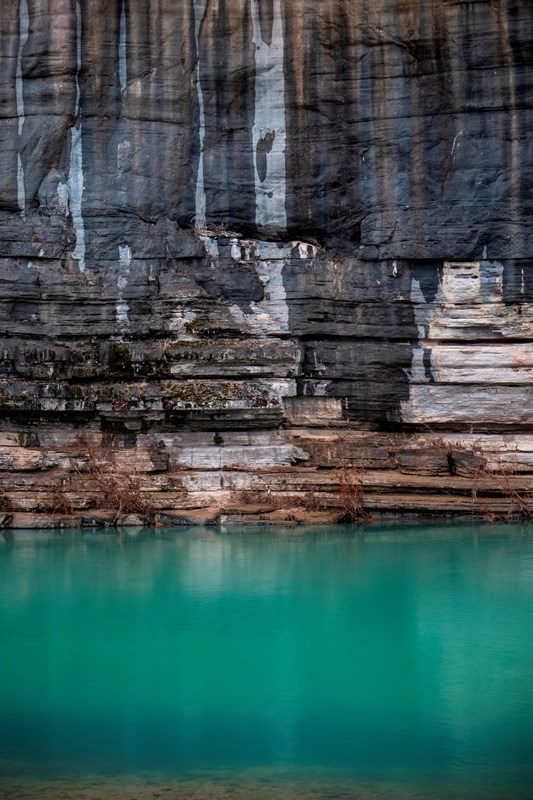 Layers of rock with a turquoise river at the base.