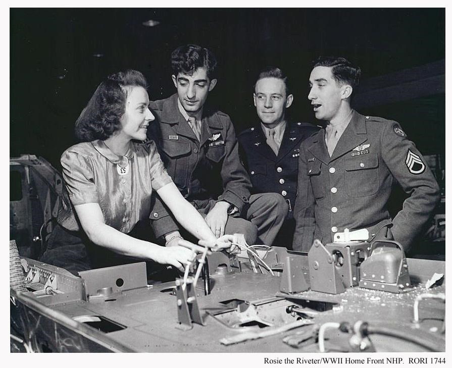 A woman and three men in WWII uniforms looking a layout.