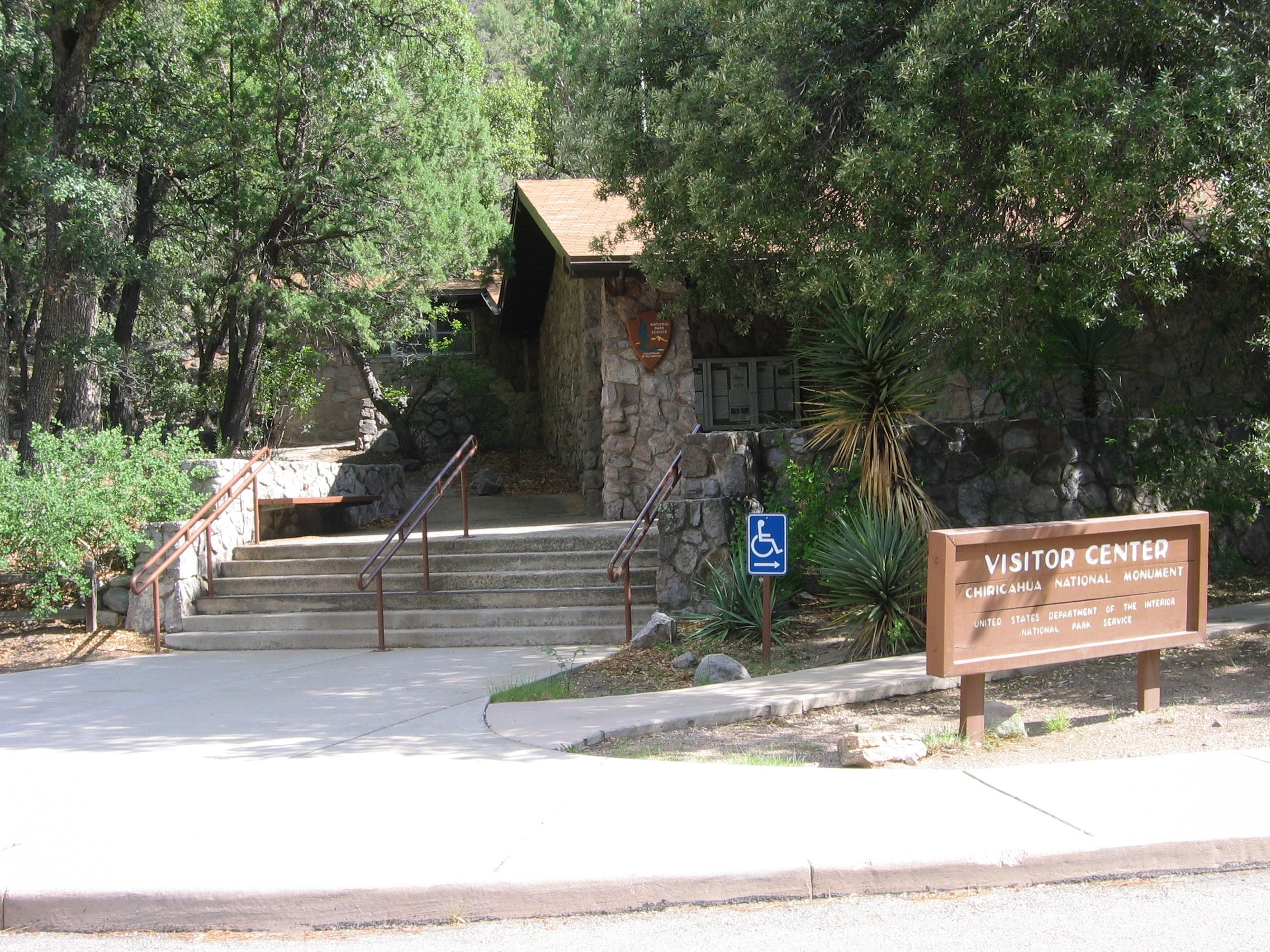 Stone built building surrounded by trees, with steps leading to the entrance and a wooden sign.