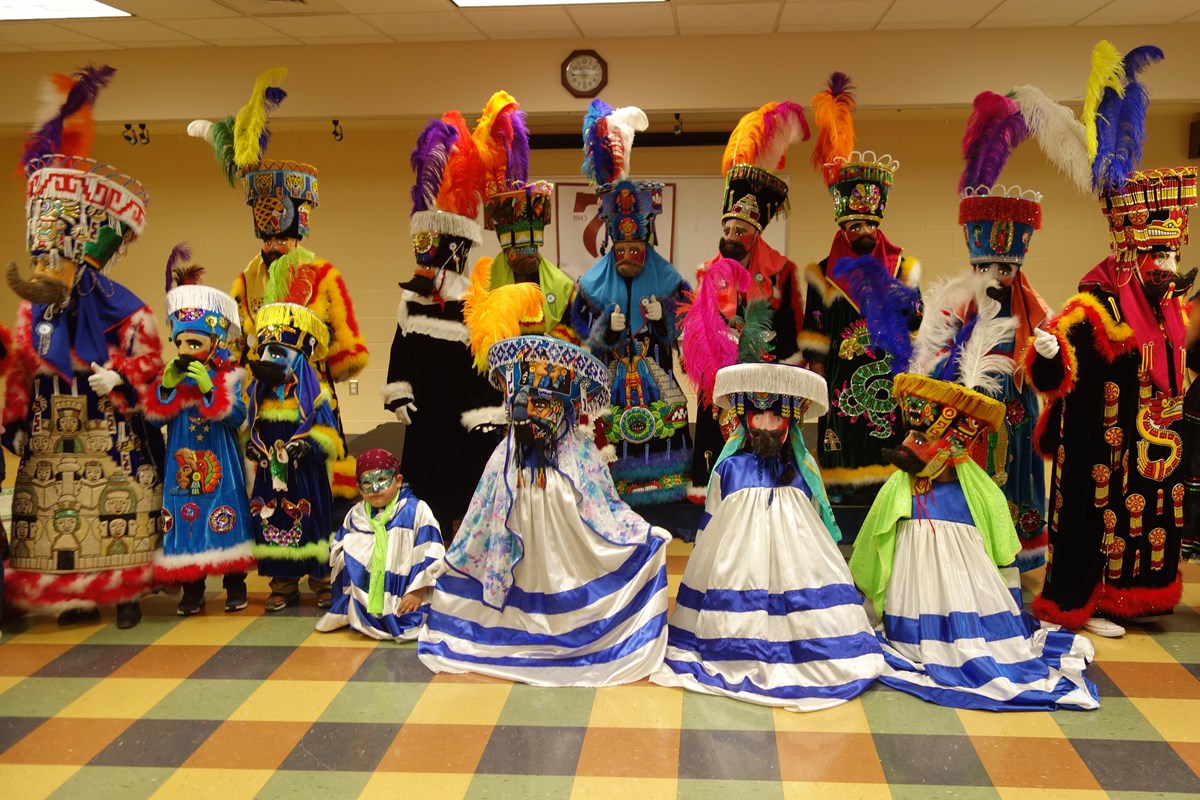 15 individuals dressed in colorful costumes and hat pieces.