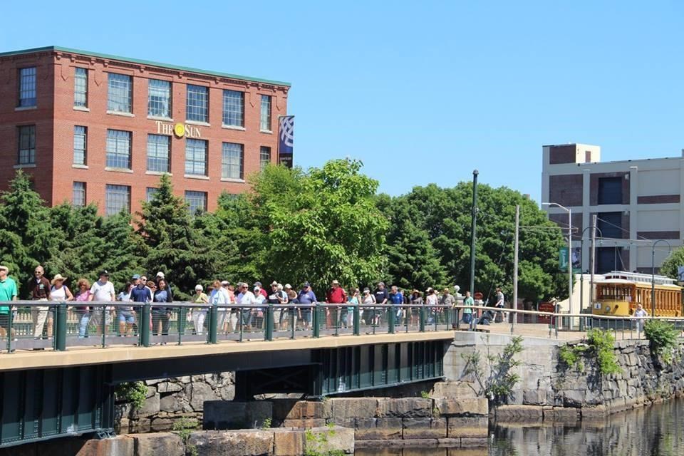 Group of visitors walking along pedestrian bridge over canal in downtown Lowell.