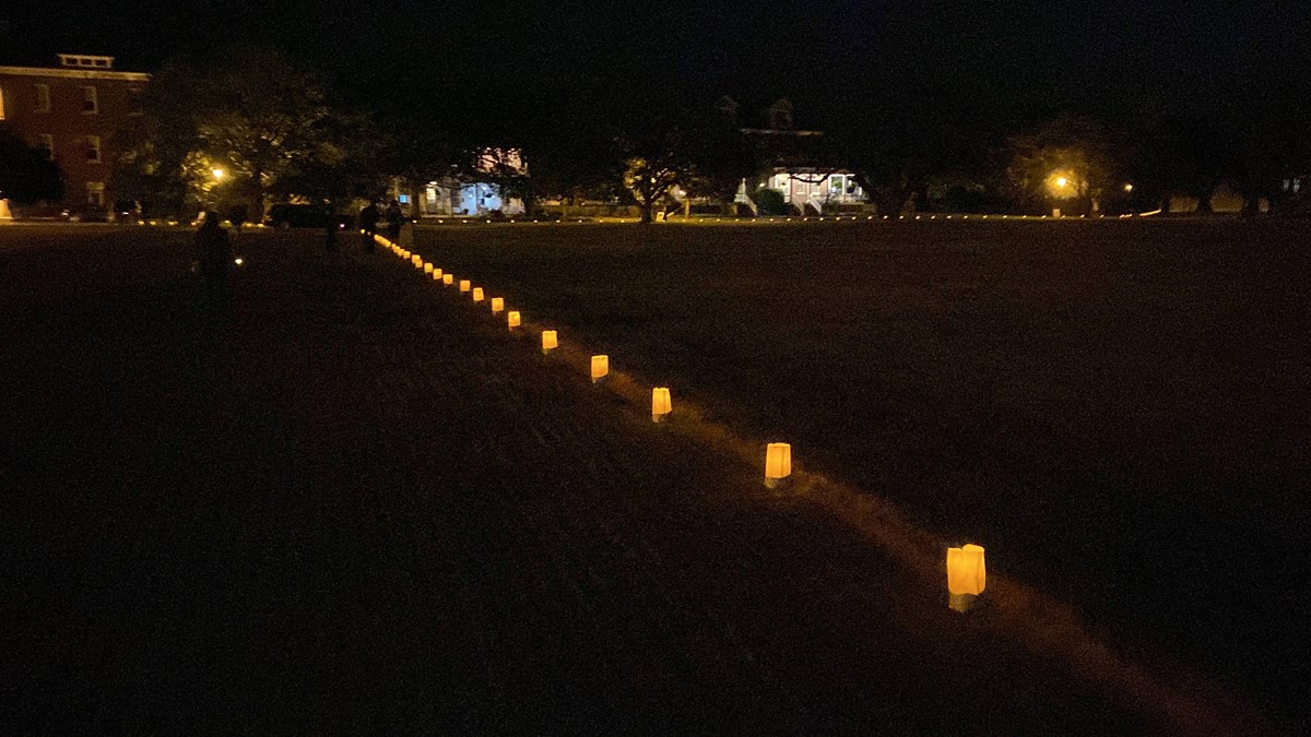 Dark night with a line of candle lights in white bags spaced on the ground in a line.