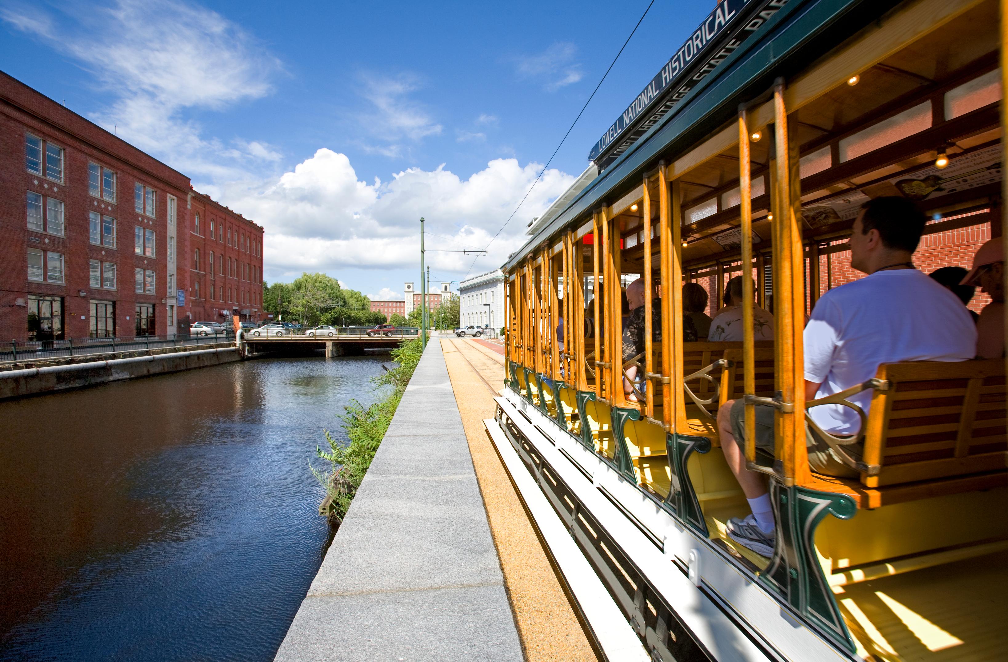 A historic trolley travels alongside a filled canal with a brick building on the other side.