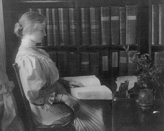 Helen Keller seated, right profile, reading braille.