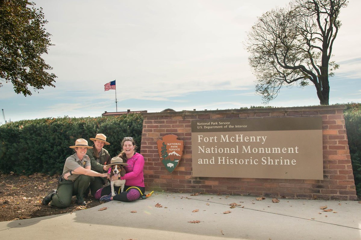Park Rangers with visitor and dog in front of park sign.