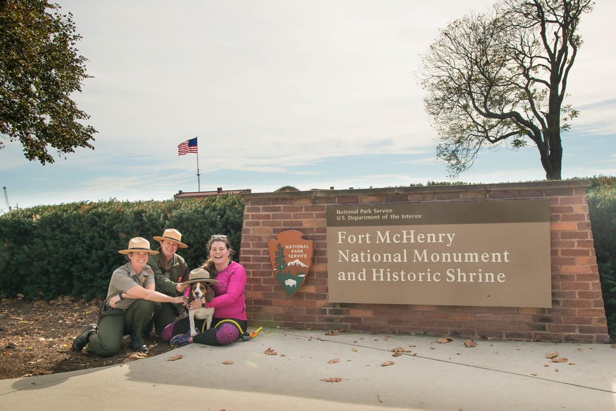 Park Rangers with visitor and dog in front of park sign.