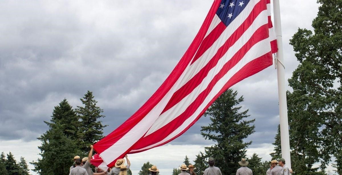 US flag being hosted up the flagpole by National Park Service employees and community members.