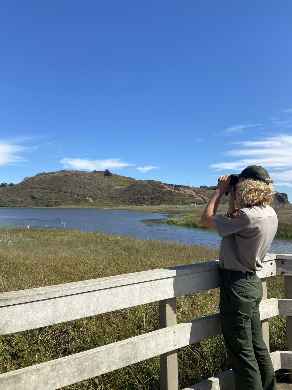 A ranger uses binoculars to look for birds at Rodeo Lagoon.