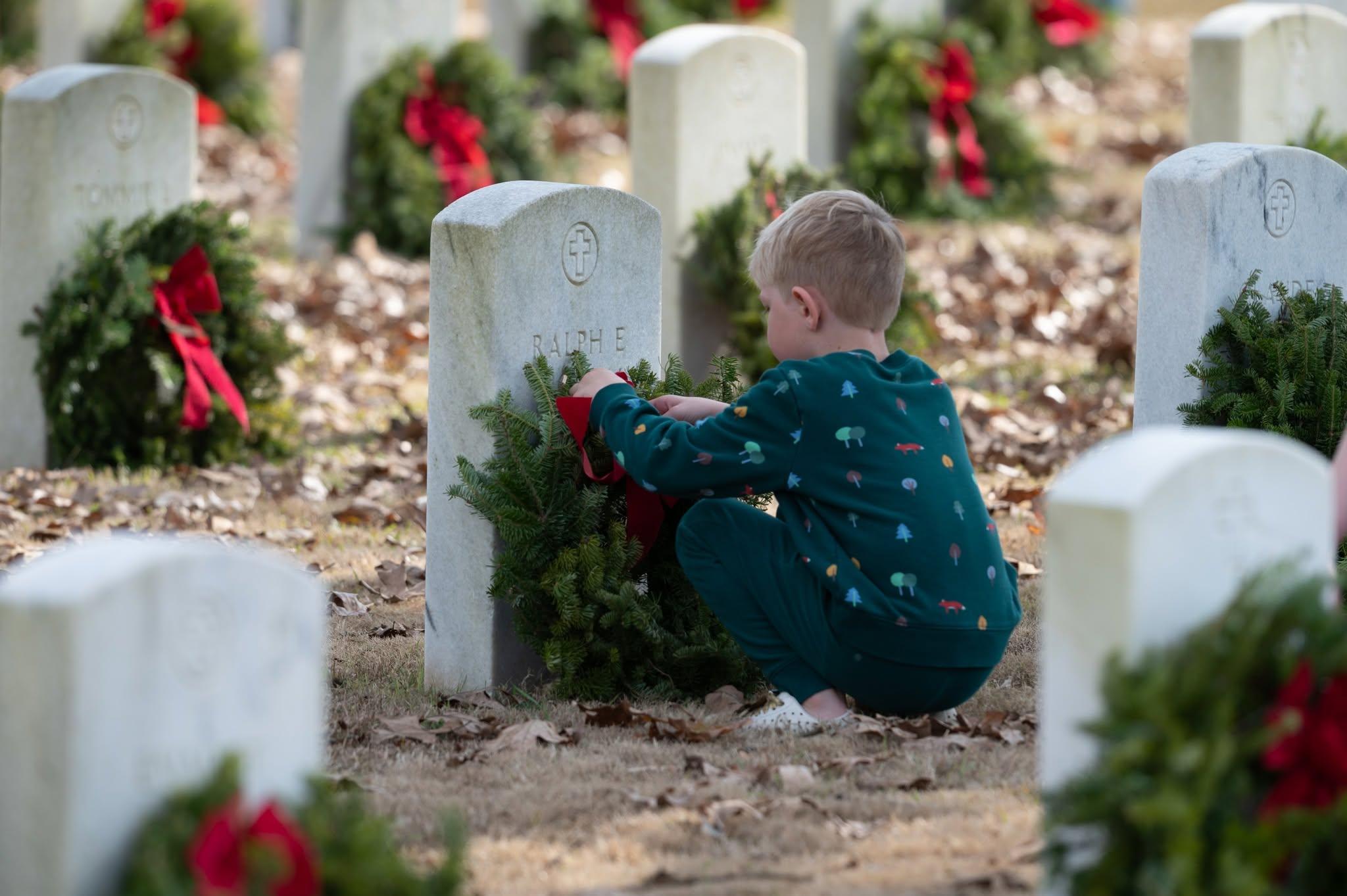 Small child placing wreath on white marble headstone.