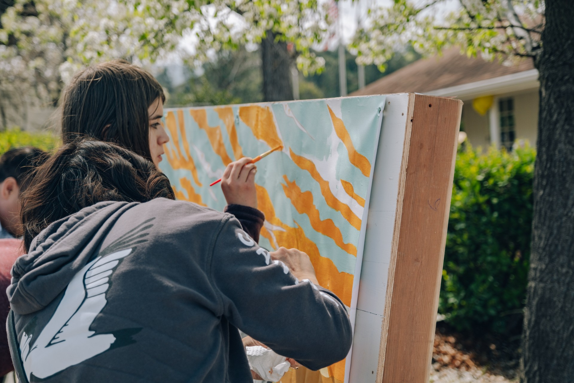 photo showing two people painting orange and light blue shapes on a canvas outdoors