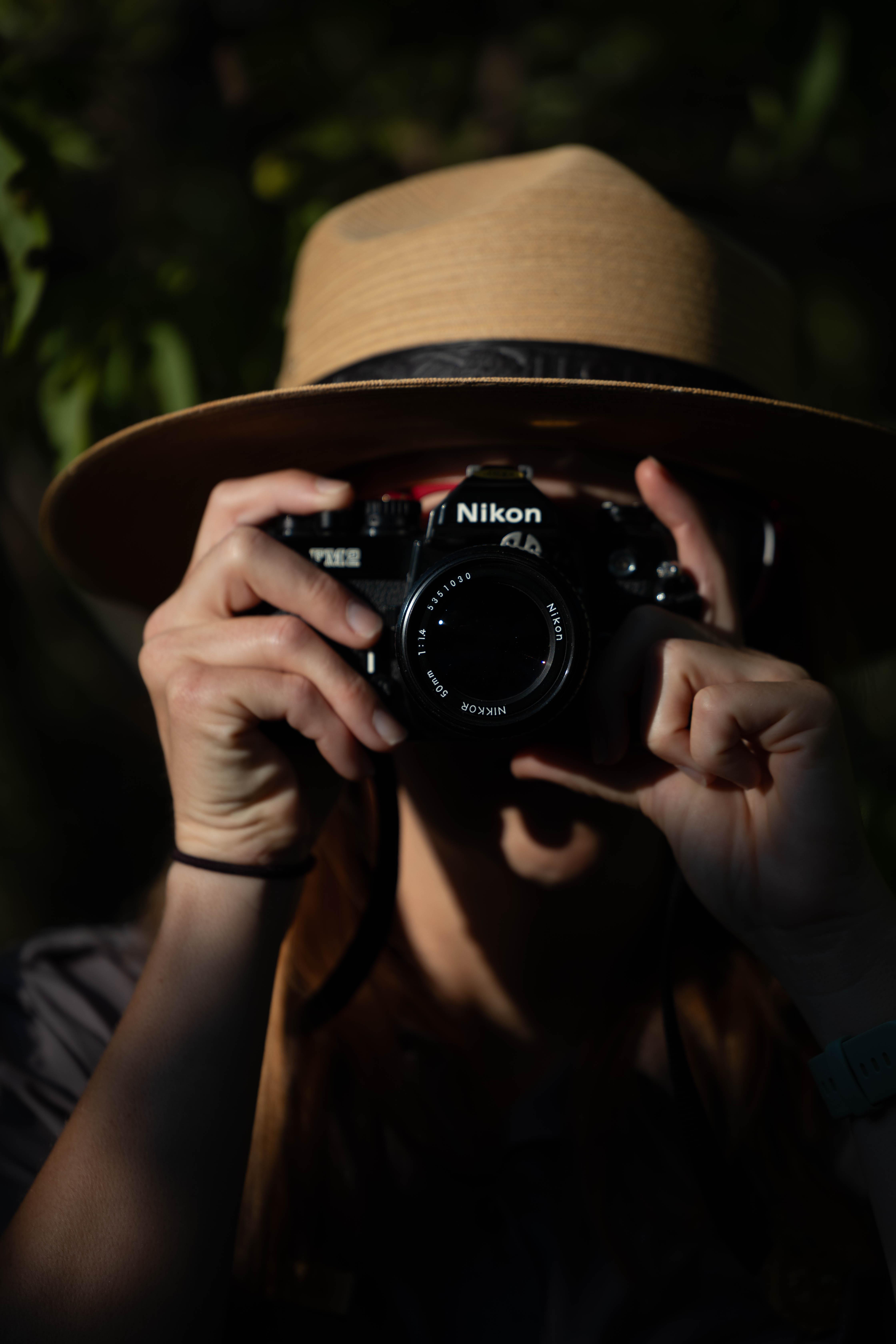 A person wearing a wide-brimmed hat holds a camera up to their eye, poised to take a picture.