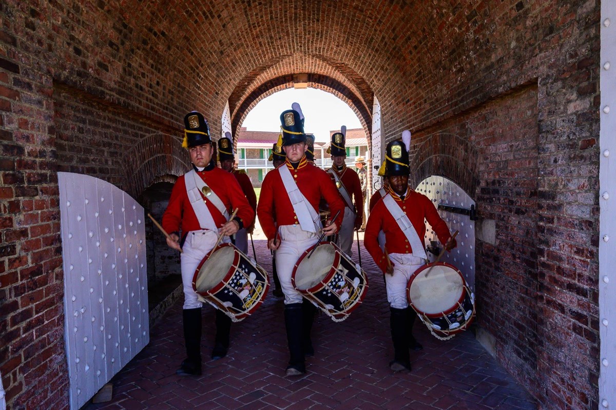War of 1812 musicians in red march through Fort McHenry sally port