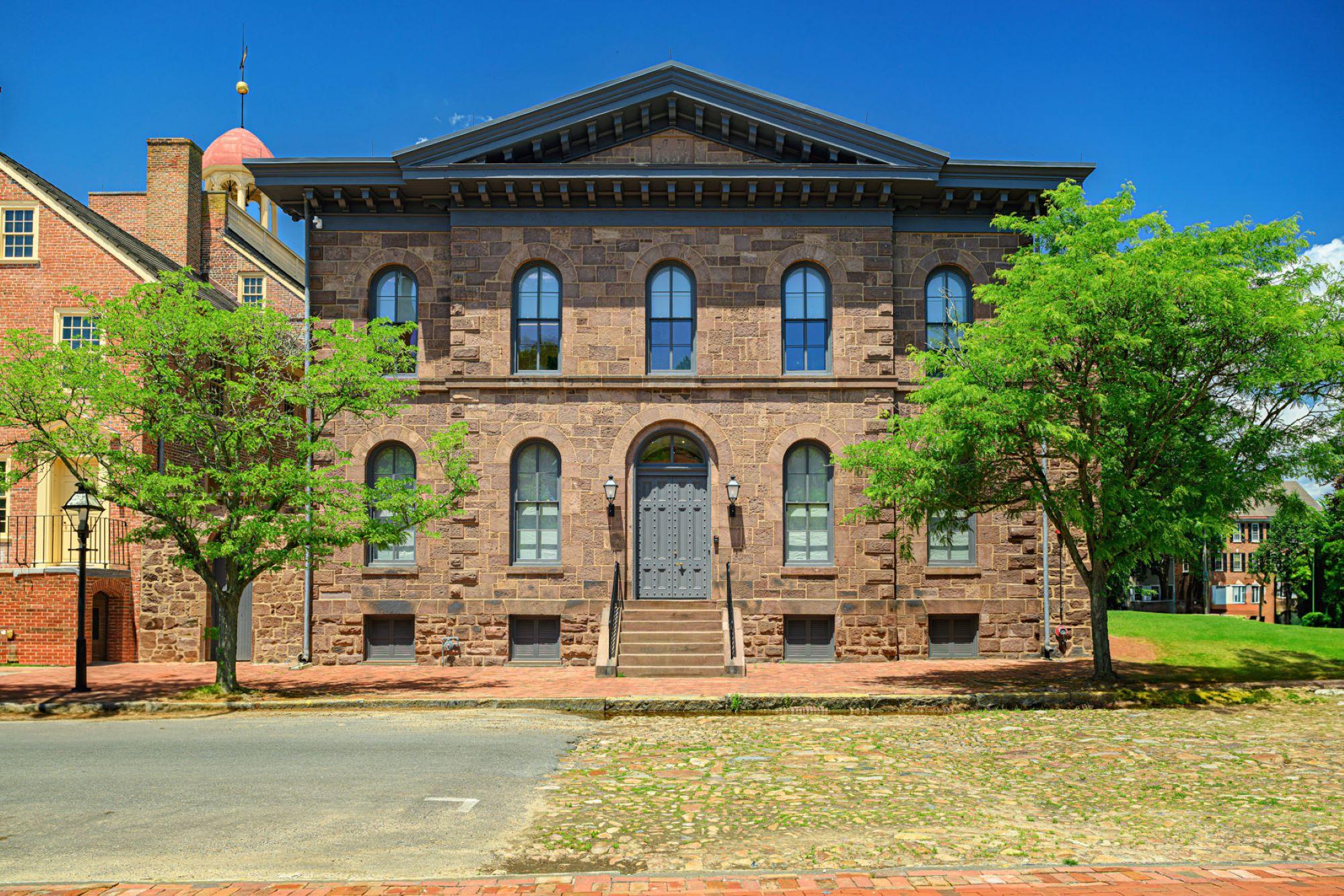 Two story brown stone building on a cobblestone street.