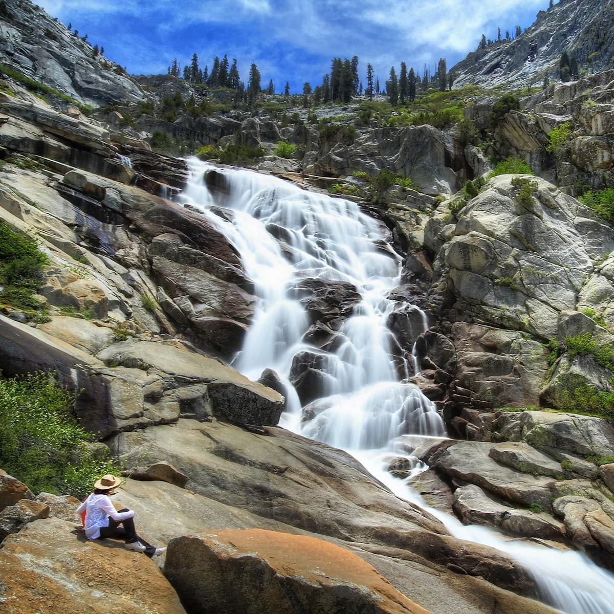 A woman rests on a rock next to a cascading waterfall.