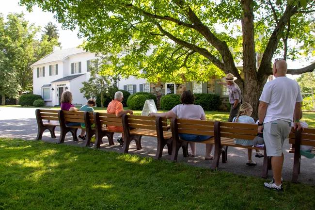 A group of visitors sits at benches listening to a park ranger speak