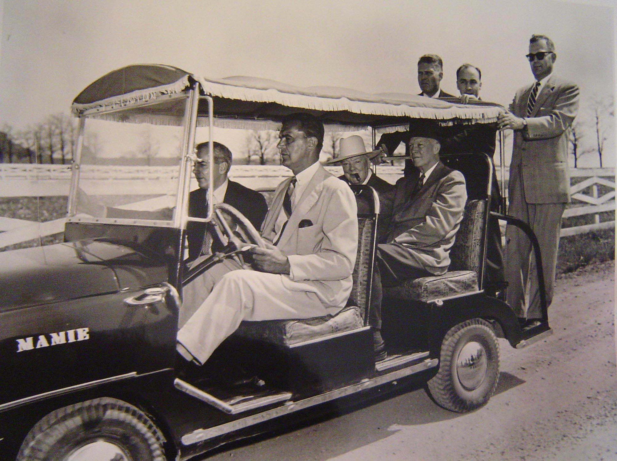 A black and white image of several people riding in a motorized golf cart