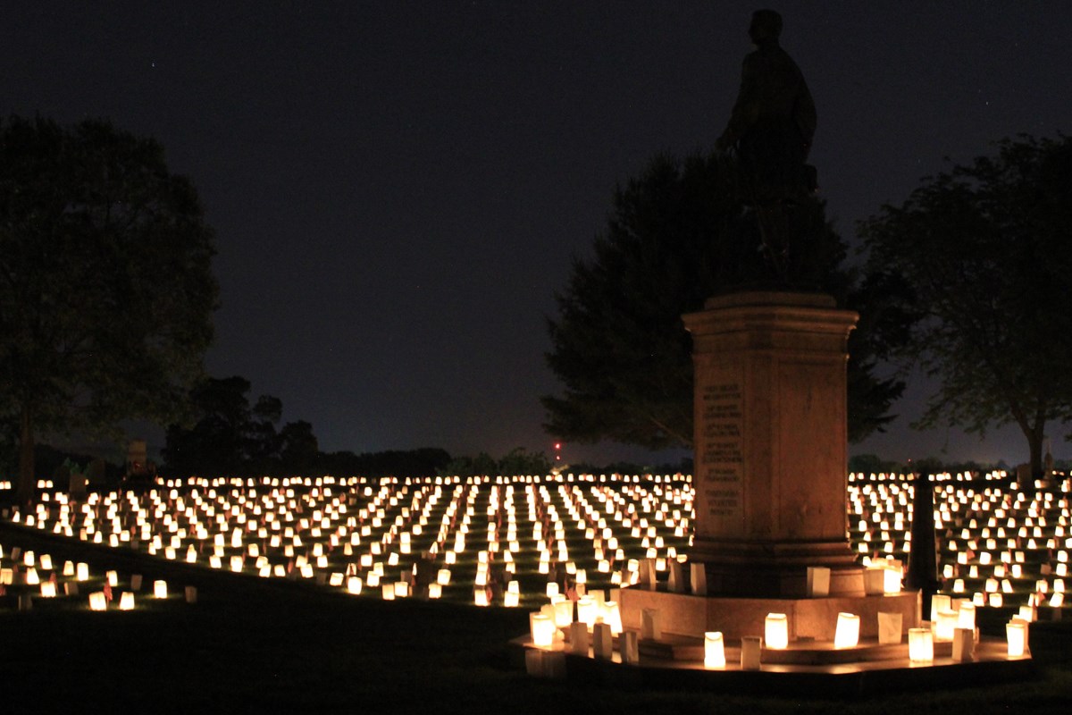 Candles surround a cemetery monument after sunset.