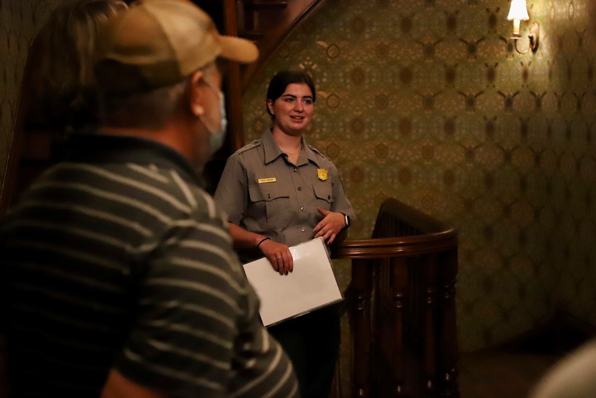 A park ranger talks to a group of people in a wallpapered hallway.