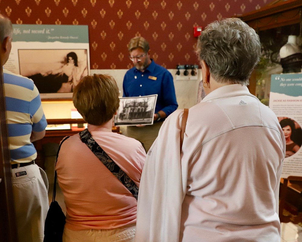 A docent begins a tour in the education center with visitors gathered around.