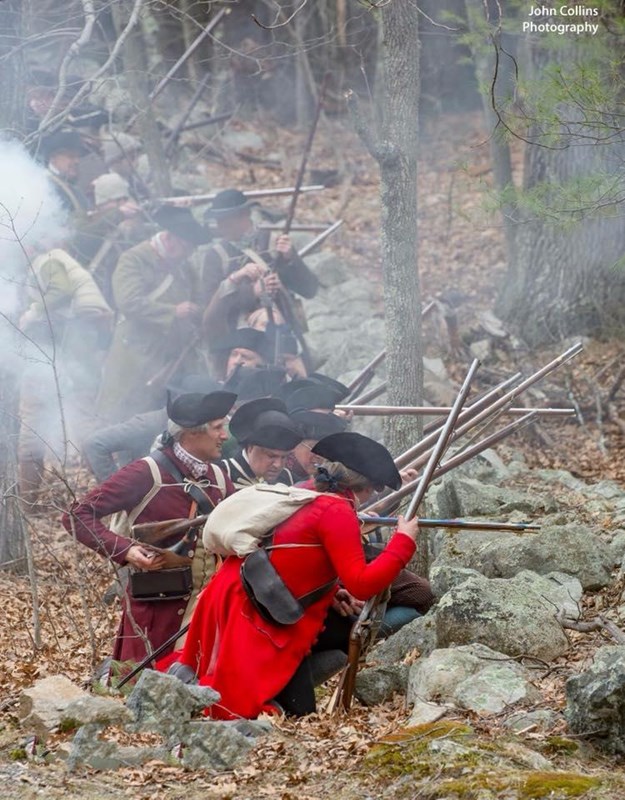 Revolutionary War Colonial soldiers take cover behind a low stone wall and fire their muskets