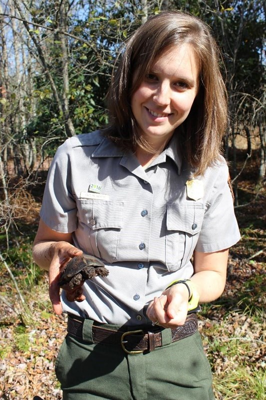 A park ranger holding a turtle smiles into the camera