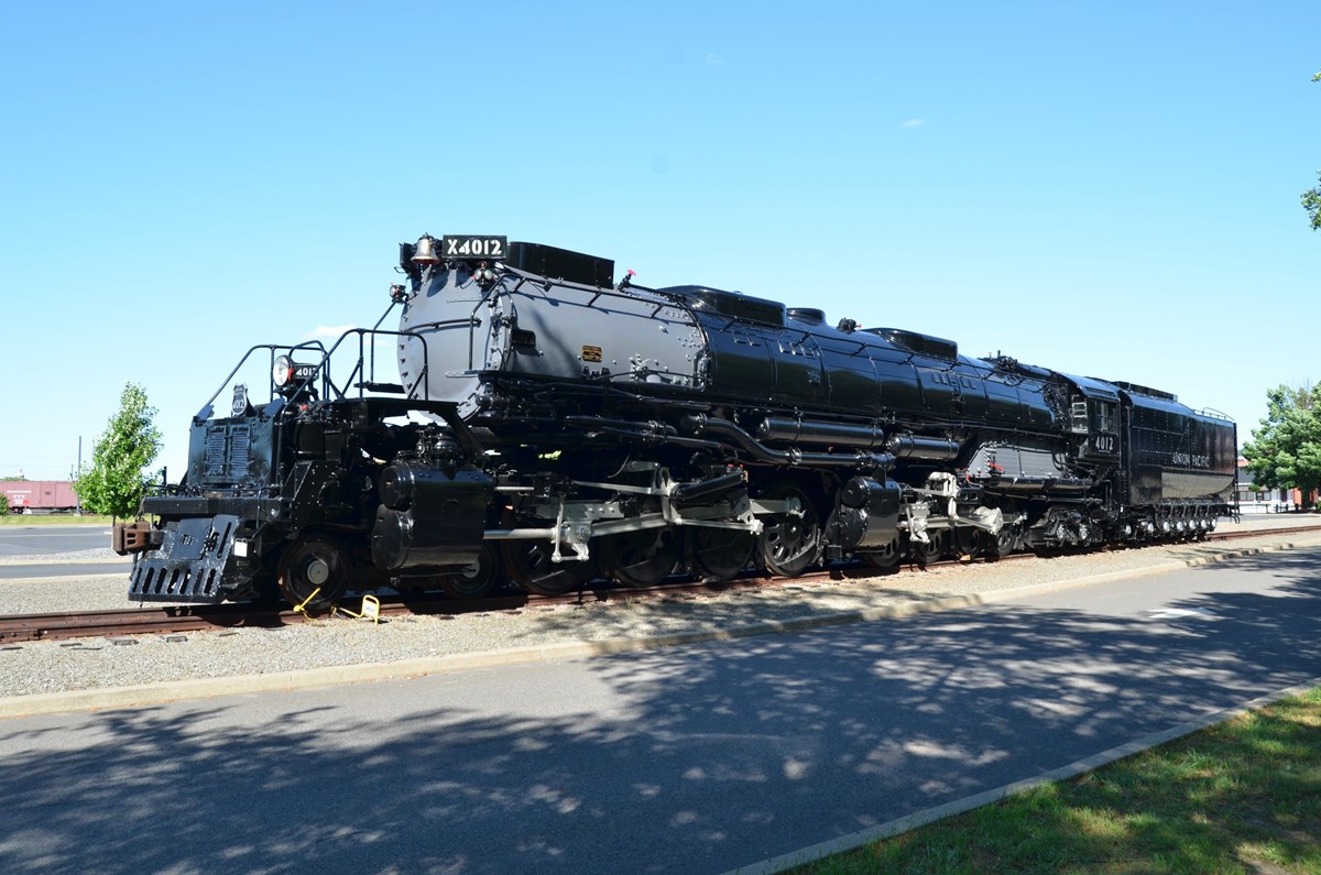 Large locomotive painted mostly black rests on track adjacent to parking lot