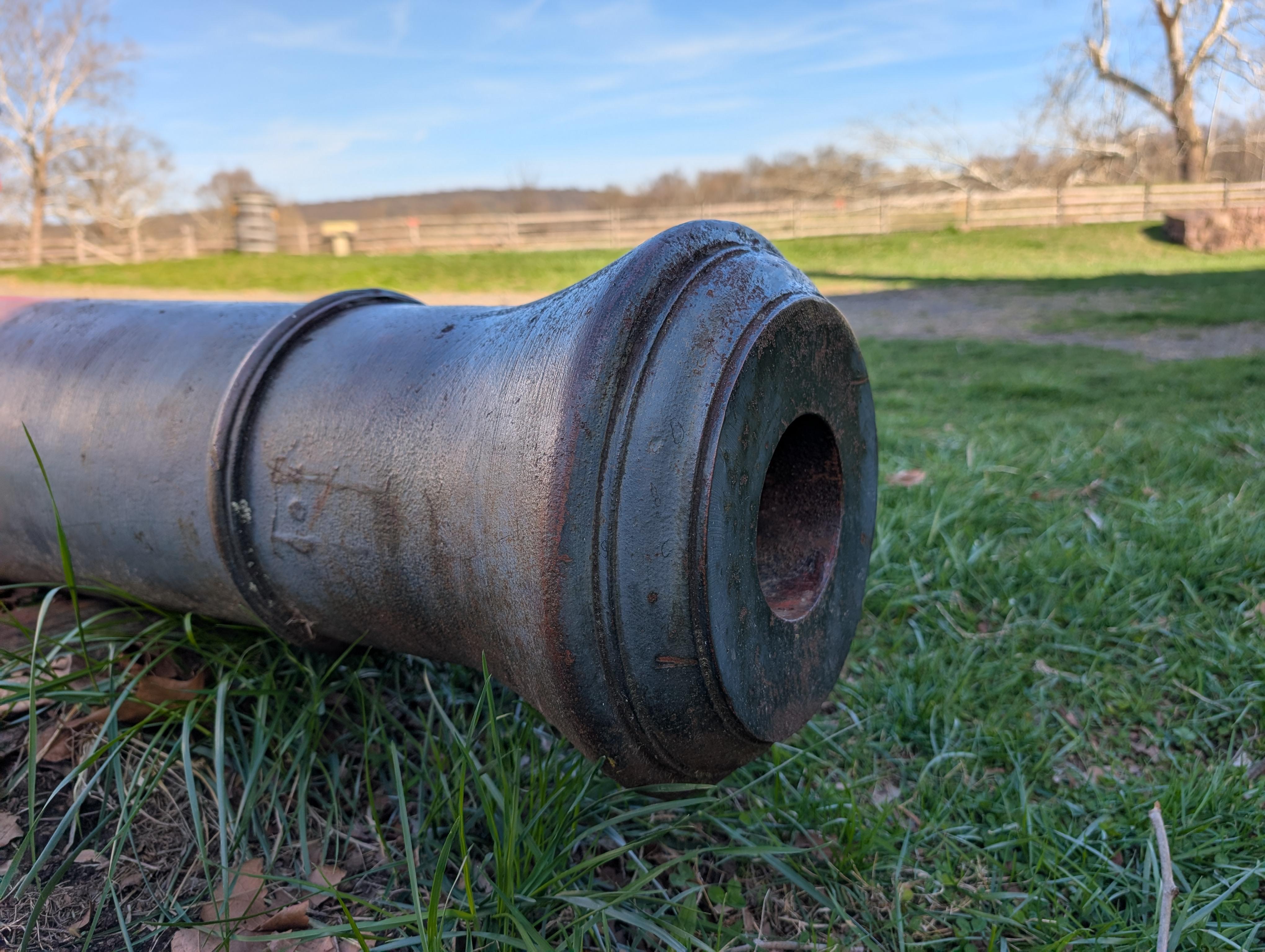 Close-up of the front part of a cannon barrel sitting on a patch of grass.