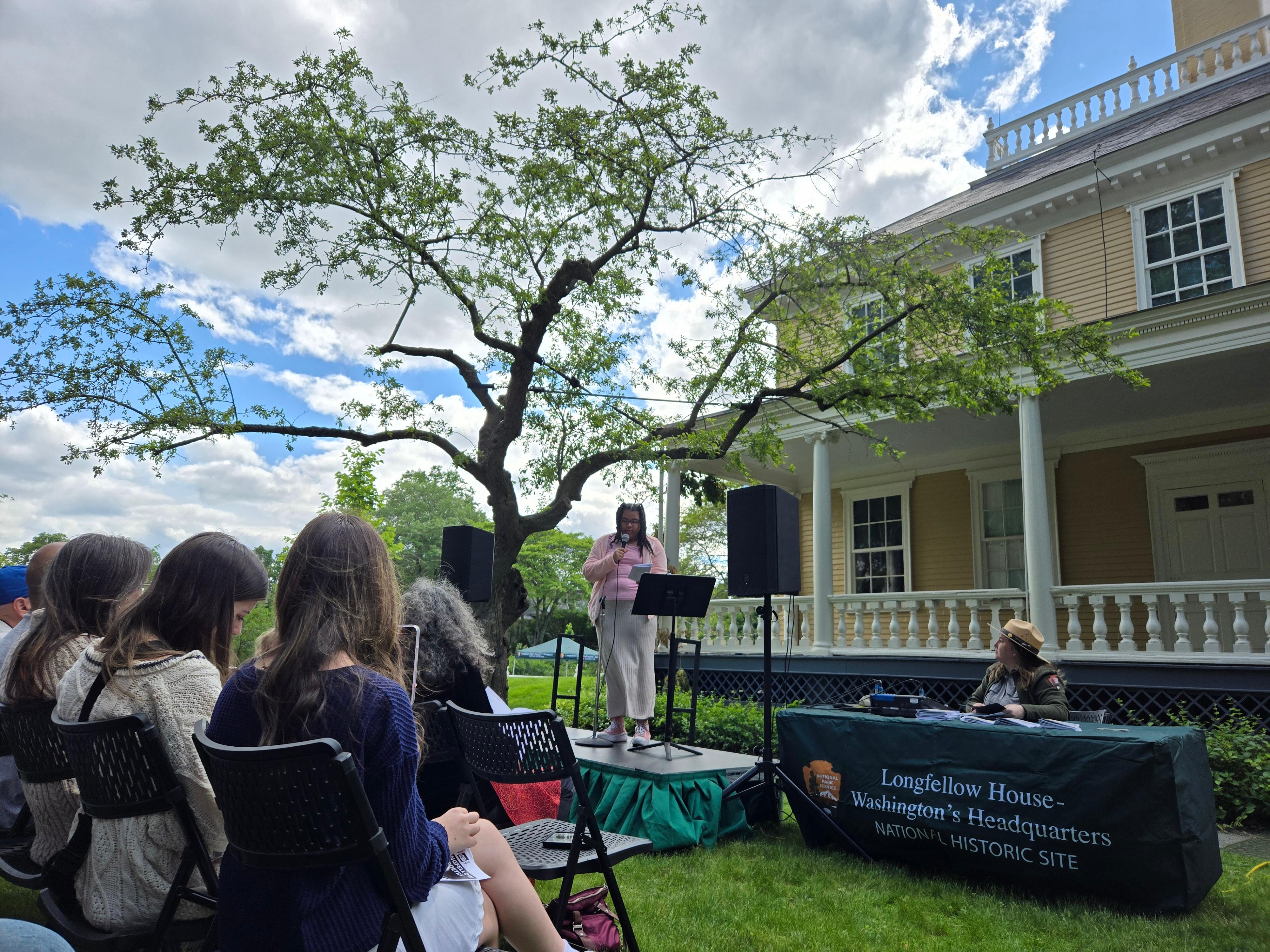 Young poet reads on an outdoor stage as audience looks on