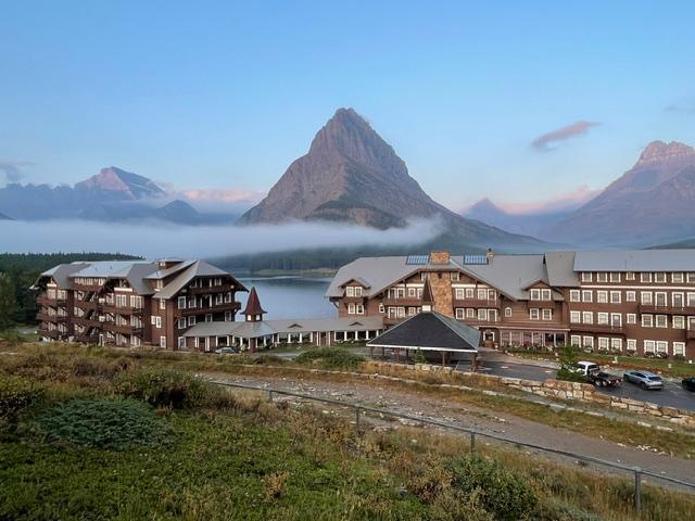 exterior view of 4-story hotel with clipped gables, dormers, balconies and mountain and lake beyond
