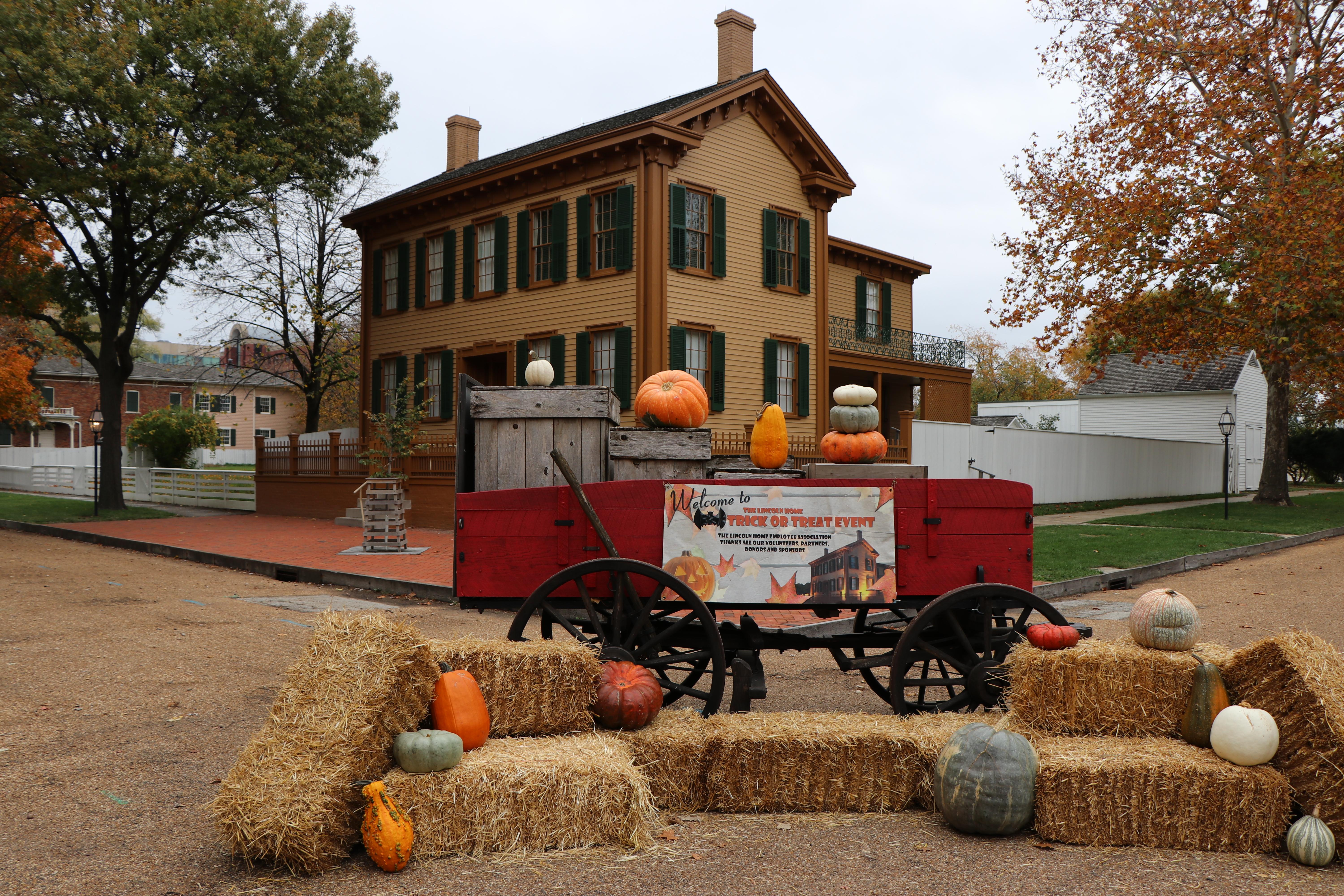 Image of the Lincoln Home with a wagon in front. There are pumpkins and hay bales set decoratively