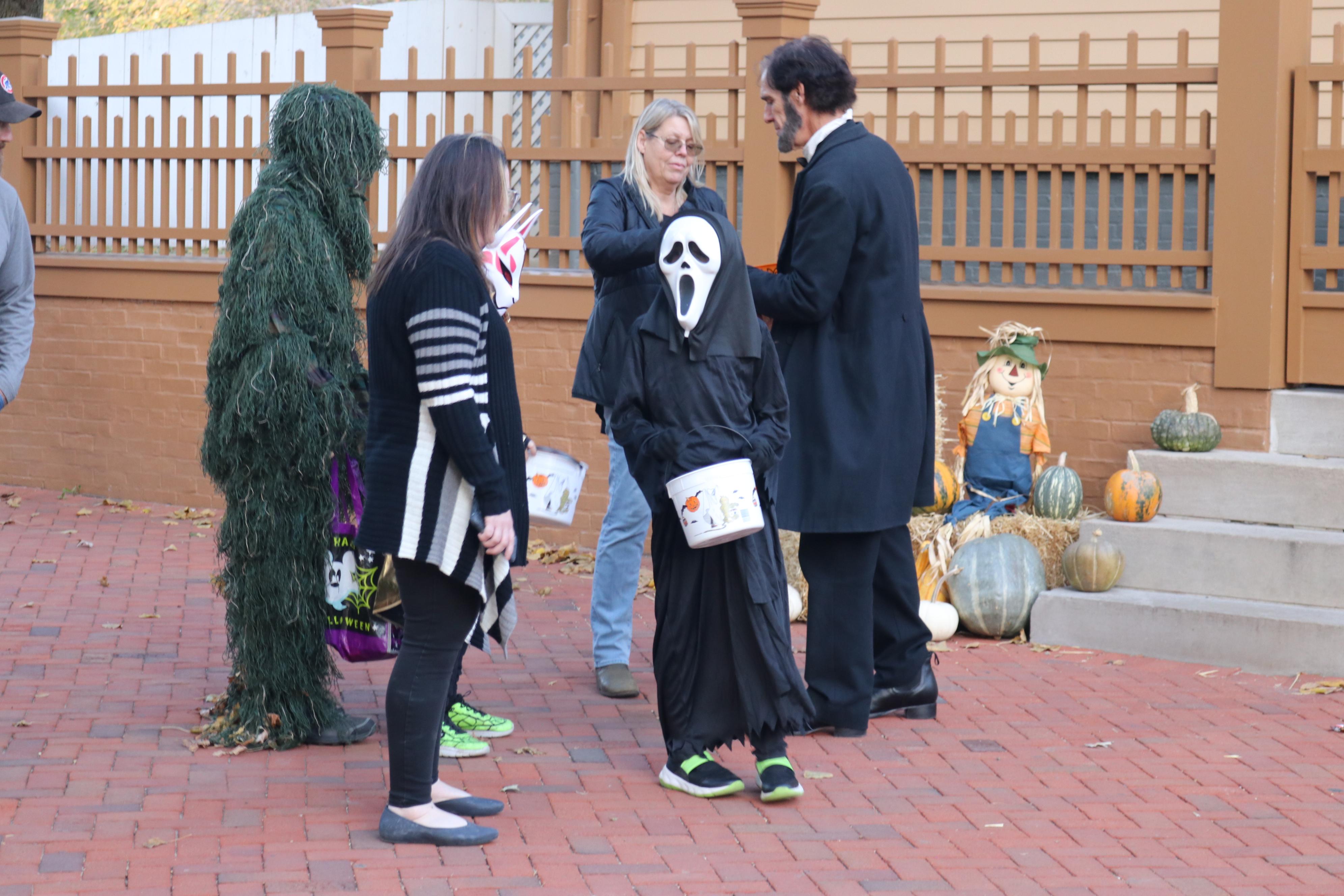 Image of Abraham Lincoln in front of his home with 4 visitors, 3 of whom are dressed in costumes.
