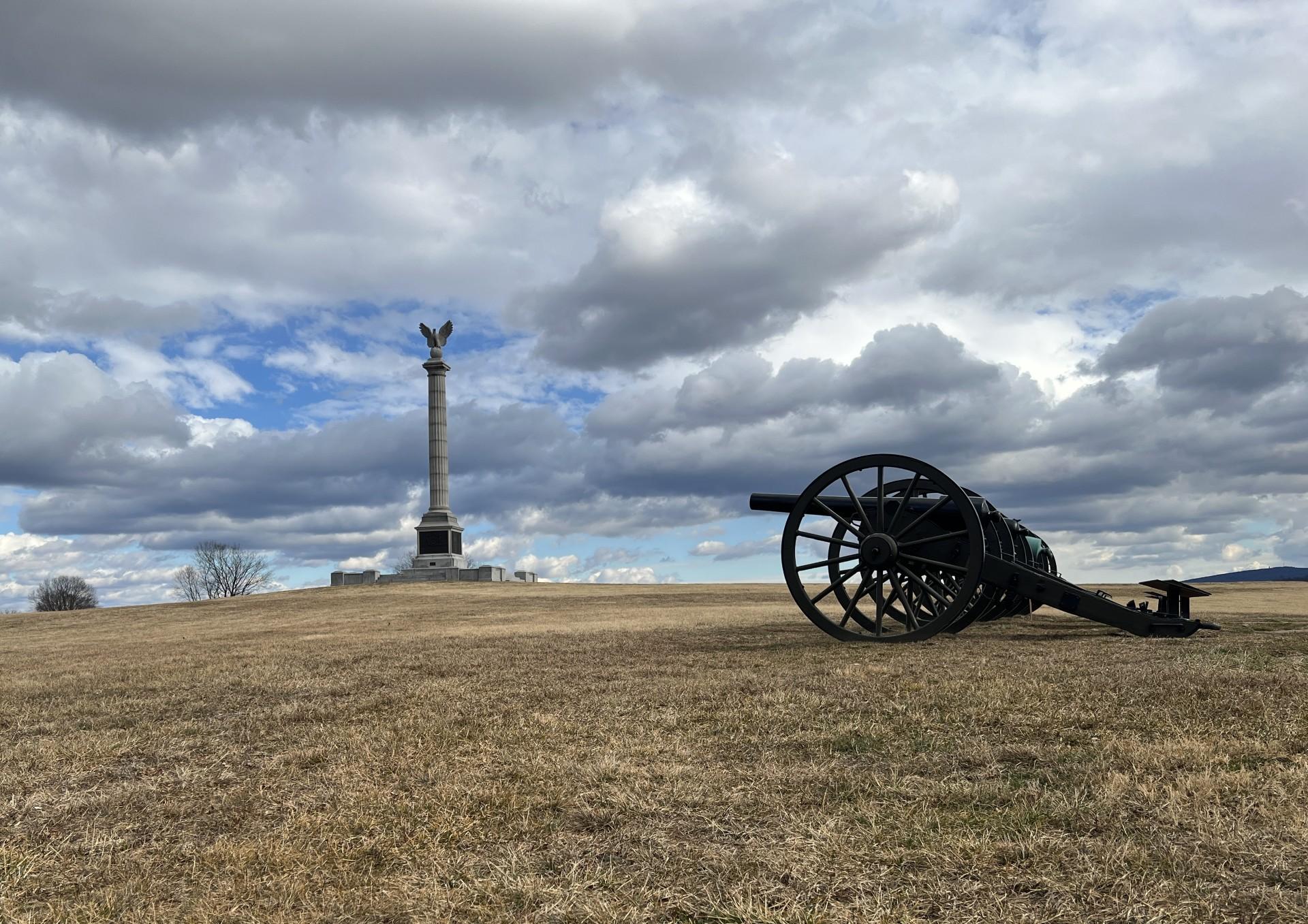 cannon with tall monument and dramatic sky