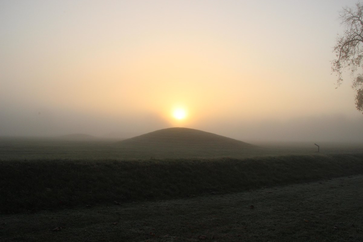 a foggy sunrise behind an earthen mound.