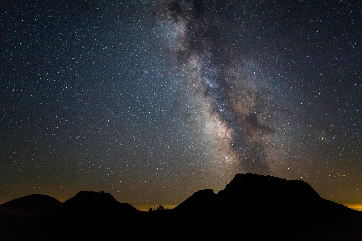 the milky way and a night sky full of stars over the silhouettes of several small volcano cones
