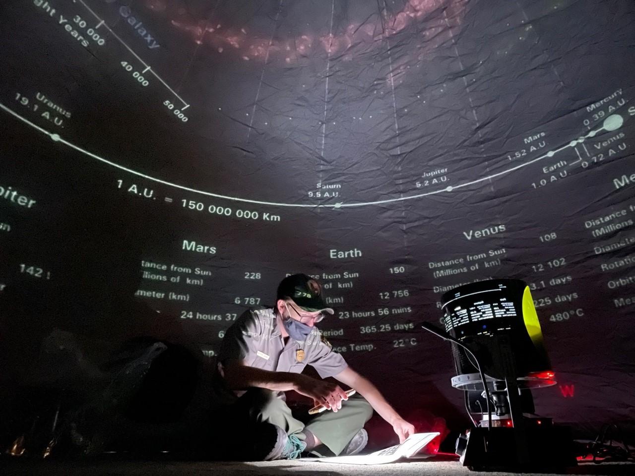Ranger sits under a timeline projected onto dark planetarium wall