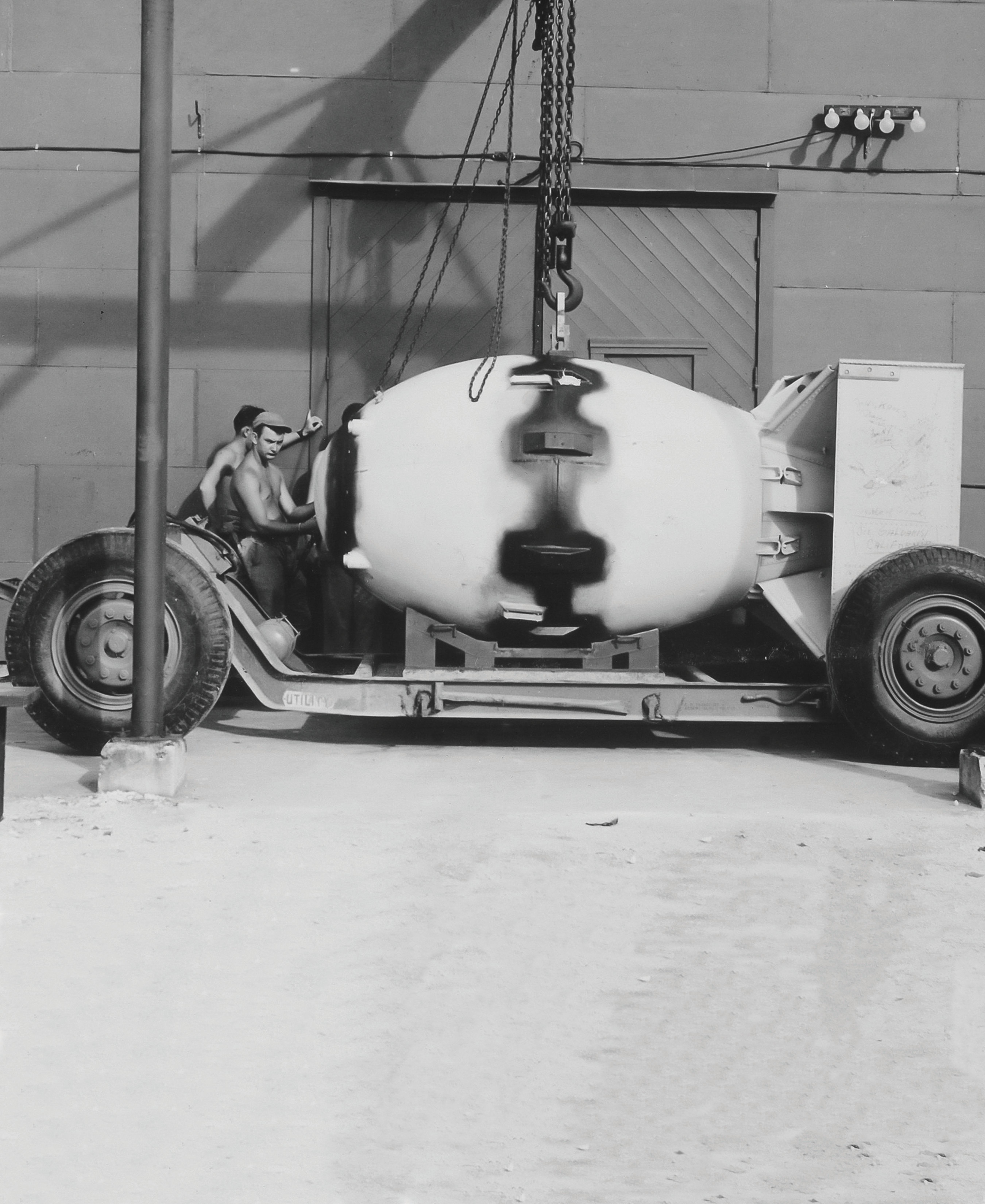 Two men maneuver a vehicle with a large white contraption suspended by a hook.