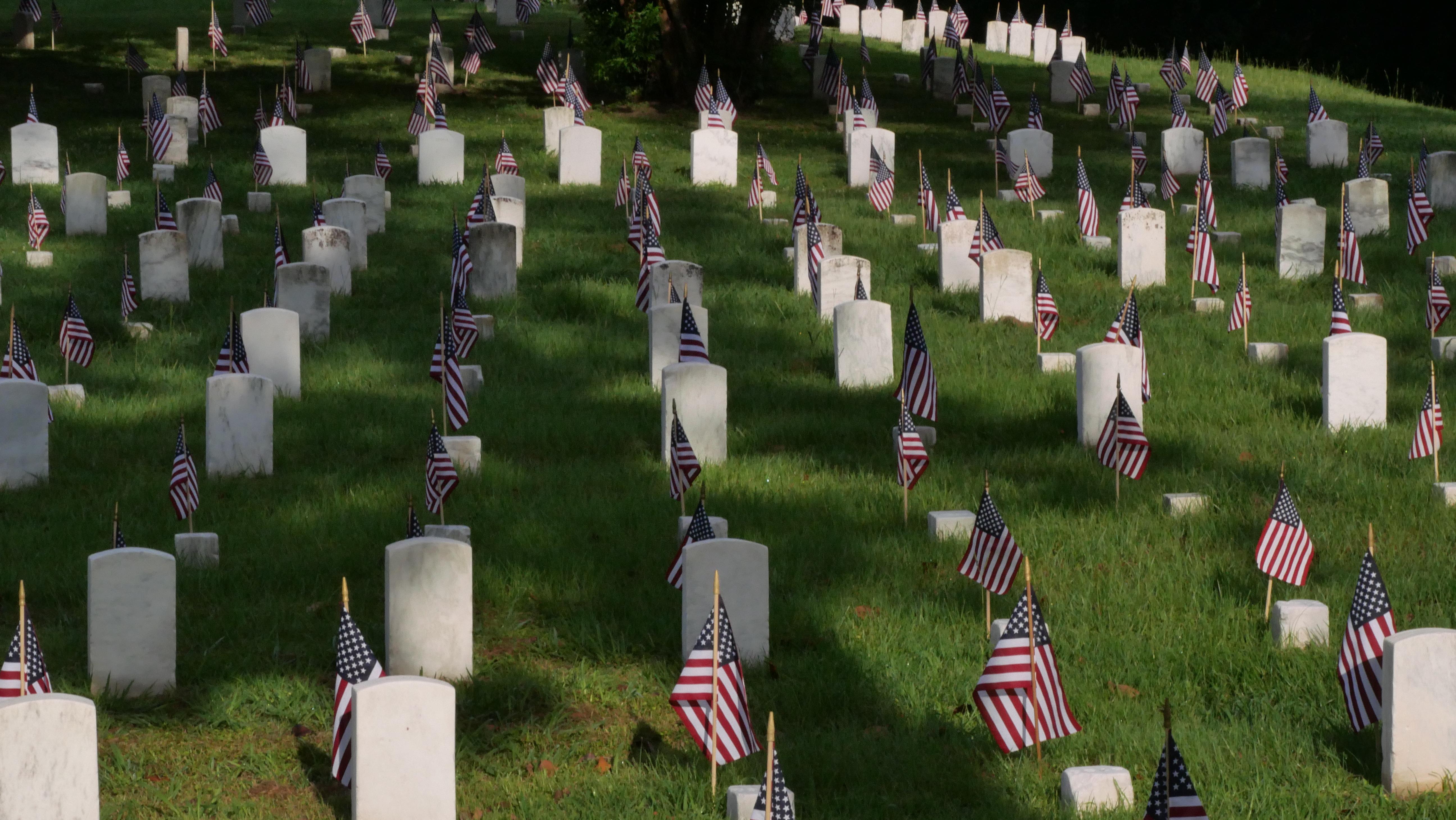 White stone grave markers in green grass with US Flags at each grave marker