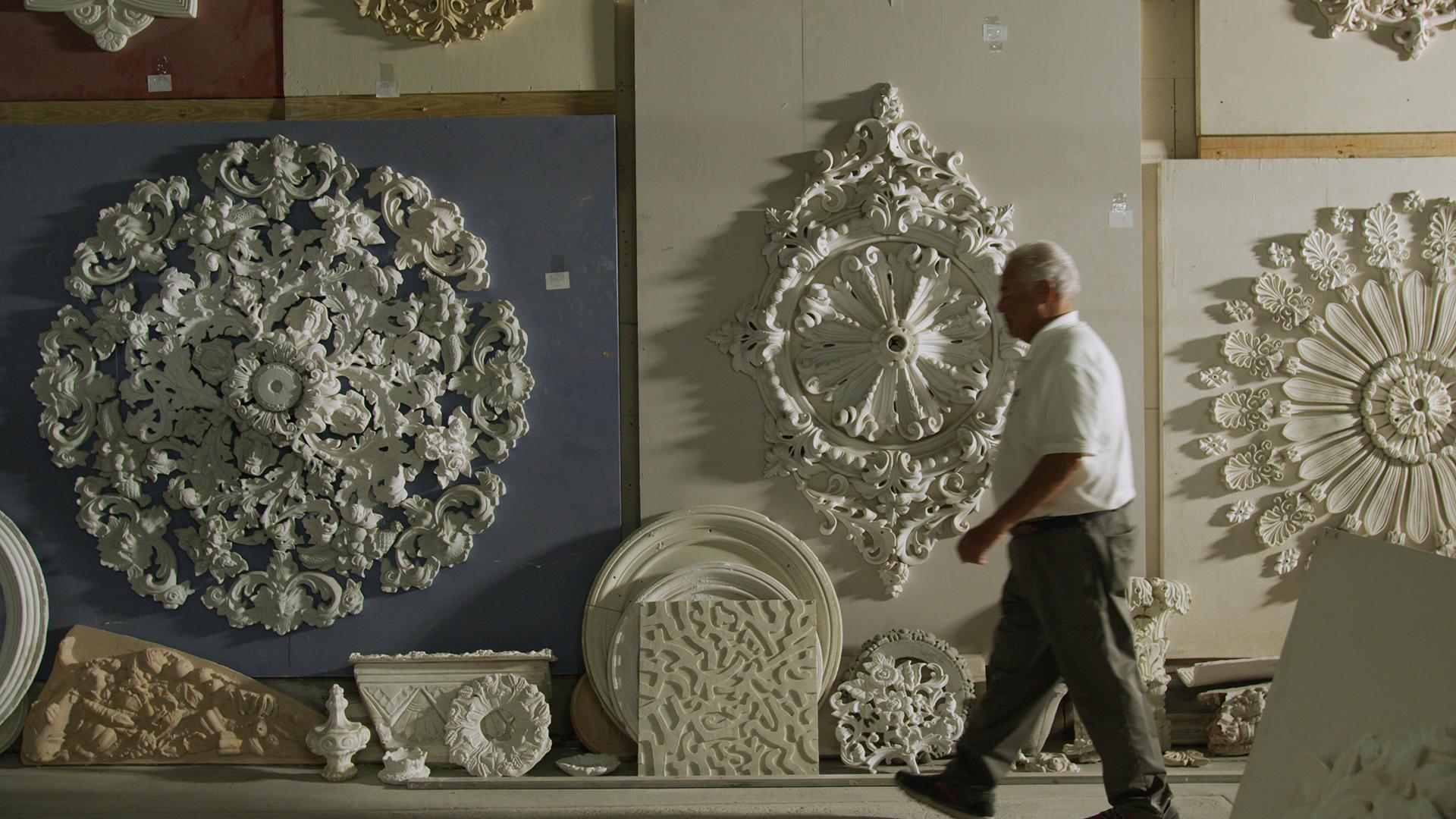 A man walking in front of several plaster ceiling medallions.