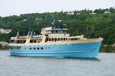 Ranger III cruising the Keweenaw Waterway with a forested hillside behind it.