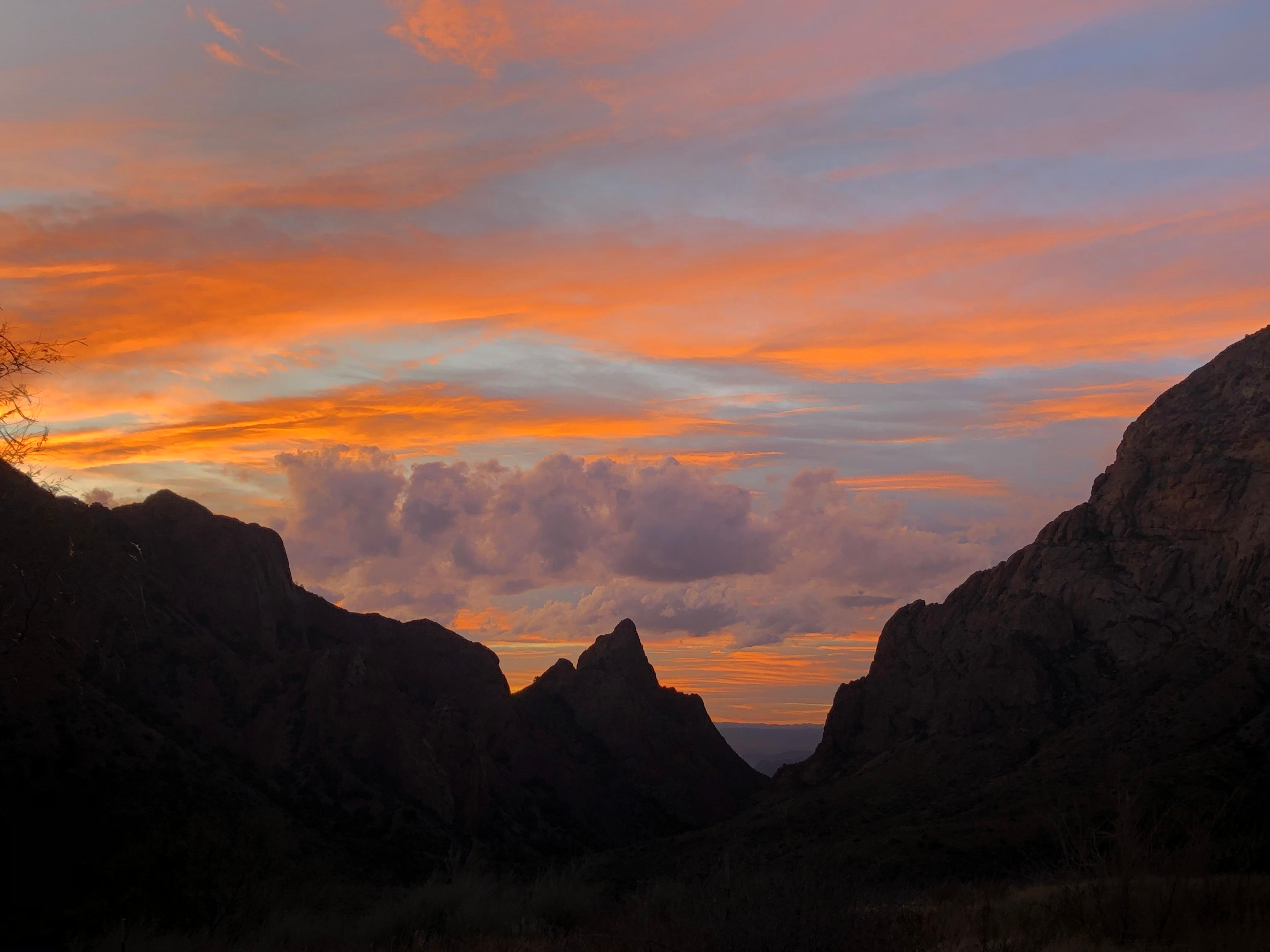 Silhouetted desert mountain vistas with a setting sun and vibrant clouds in shades of red and orange