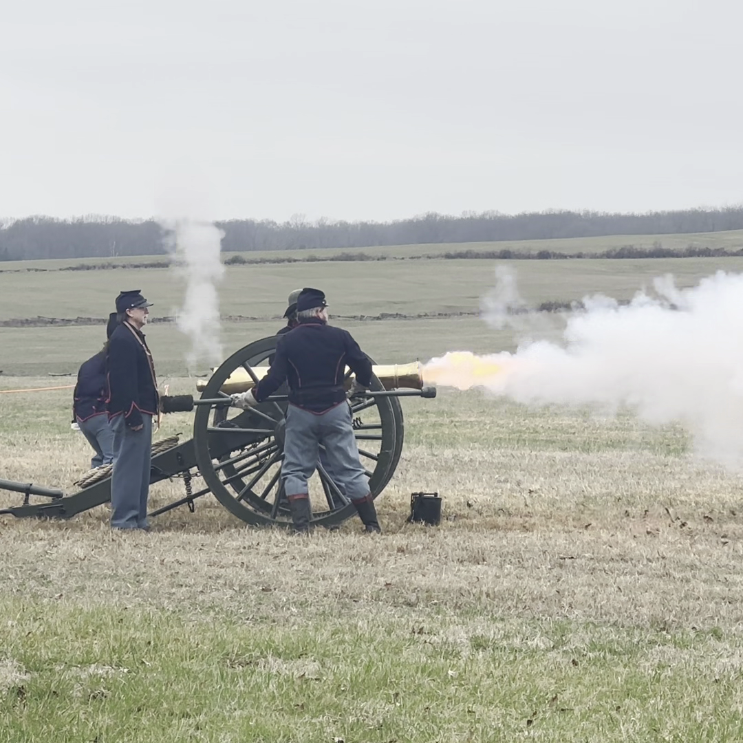 Back ground rolling fields, middle ground cannon, white smoke and four cannoneers' around cannon.